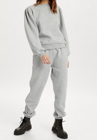Light gray sweatshirt with puff sleeves and ribbed cuffs, paired with matching sweatpants featuring elastic ankle cuffs. Black combat boots.