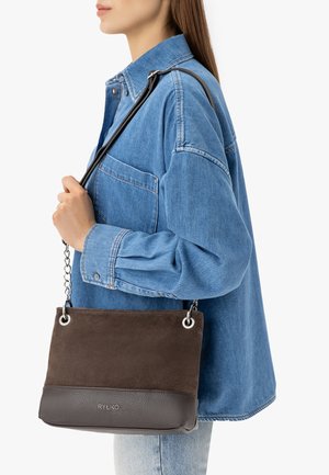 Frau in blauem Jeanshemd trägt eine braune Schultertasche aus Wildleder und Leder mit Kette und schwarzem Riemen.