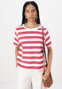 Camiseta a rayas rojas y blancas con mangas cortas y cuello redondo, combinada con pantalones claros y un bolso cruzado marrón.