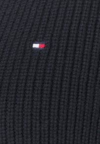 Tissu en tricot côtelé noir avec un petit logo rectangulaire brodé aux couleurs blanc, rouge et bleu.