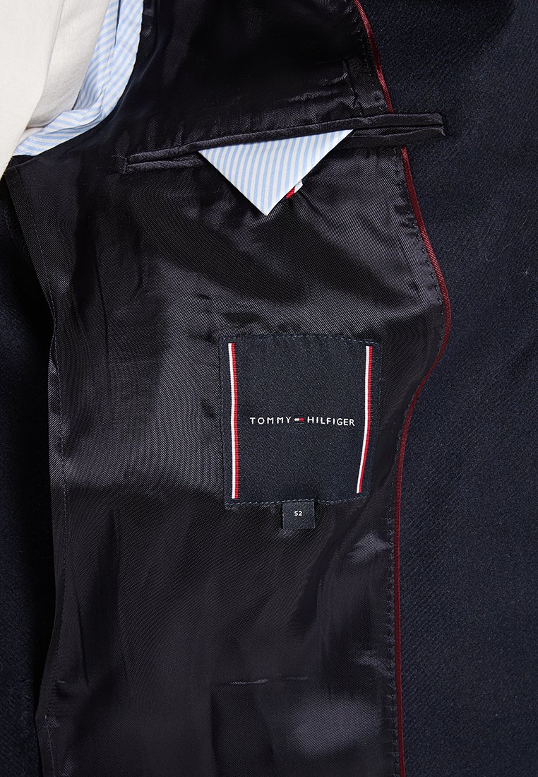 Wnętrze czarnej marynarki, z gładką satynową podszewką, kontrastującym czerwonym wykończeniem oraz niebieską i białą wąską chusteczką w kieszeni z metką.