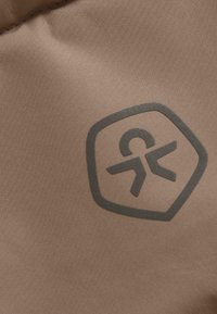 Un tejido marrón con una textura suave presenta un logo oscuro en forma hexagonal. El logo incluye una figura estilizada y acentos abstractos.