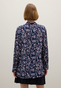 Langärmliges Hemd in Marineblau mit einem weißen und roten Paisley-Muster, mit einem Kragen und entspannter Passform, getragen mit einem plissierten schwarzen Rock.