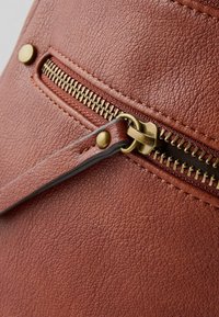 Smeđa kožna torba s vidljivim mesinganim patentnim zatvaračem i hardverom. Tekstura je grublja, a detalji šivanja su istaknuti.