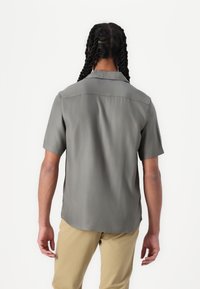 Short-sleeve gray shirt made of smooth fabric, featuring a collar, side slits, and a rounded hem. Worn with light beige pants.