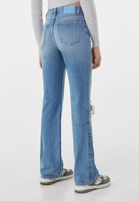 Ljusblå denimflared jeans med ett slitet detalj på vänster ben, fem fickor och en läderliknande logotyp på baksidan.