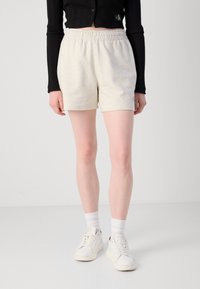 Lyse grå bomullsshorts med elastisk liv, med en subtil logo-detalj. Kombinert med hvite joggesko og hvite sokker i crew-lengde.