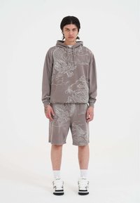 Grau Pullover-Hoodie und passende Shorts mit einem weißen Drachen- und Wolkenmuster, aus einem weichen Material, getragen mit weißen High-Top-Sneakern.