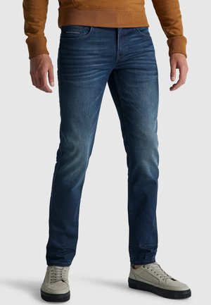 Schmal geschnittene, dunkelblaue Jeans mit leichter Verwaschung, fünf Taschen und mittelhoher Taille. Kombiniert mit hellgrauen Sneakern.