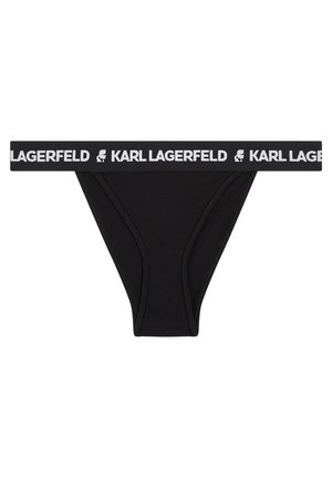 Melna tanga apakšveļa ar baltu elastīgu jostiņu, kurā ir teksts "KARL LAGERFELD" un logo. Gluda auduma, minimālisma dizains.