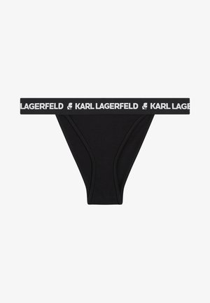 Melna tanga apakšveļa ar baltu elastīgu jostiņu, kurā ir teksts "KARL LAGERFELD" un logo. Gluda auduma, minimālisma dizains.