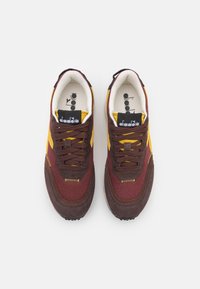 Sneaker maroon e marroni con suède testurizzato e mesh, dettagli gialli e lacci marroni. Marchio visibile sulla linguetta.