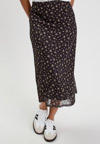 Jupe noire à fleurs avec un design fluide, ornée de petits motifs floraux et d'un ourlet transparent. Associée à des baskets blanches et grises.