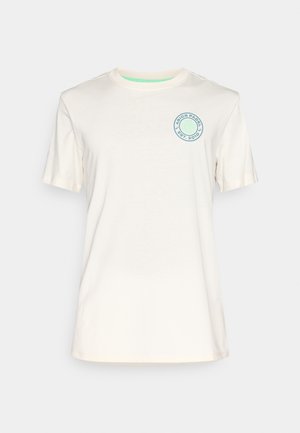 Krémové bavlnené tričko s krátkymi rukávmi, okrúhlym výstrihom a kruhovým logom v modrej farbe na ľavom hrudi. Hladká textúra, jednoduchý dizajn.