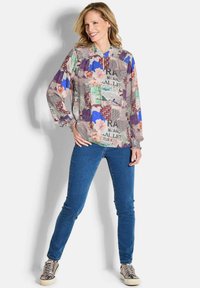Kleurige blouse met patroon in lichtgewicht stof, voorzien van losse, lange mouwen; gecombineerd met strakke blauwe jeans en metallic sneakers.