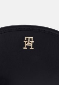 Černá kožená taška s hladkým povrchem, na přední straně s pozlaceným vyraženým logem. Šité okraje zvýrazňují design.