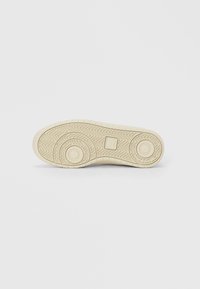 Kenkien pohja, joka on tehty kermanvärisestä kumista, ja siinä on kalanruotokuvio, pyöreät tartuntapinnat ja kuvioitu pinta. Tasaiset, pyöreät korostukset kantapään lähellä.