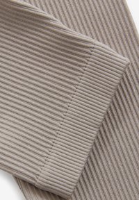 Rippierter beiger Stoff mit vertikalen Streifen, weicher Textur und einem subtilen Glanz. Detail des gesteppten Saums entlang der Kante.
