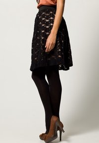 Svart spetskjol med en åtsittande midja, knälång, lagerdesign, bärs med svarta strumpbyxor och bruna högklackade skor.