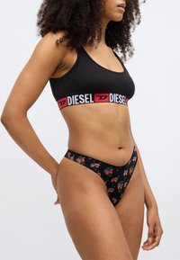 Must spordirinnahoidja punase ja valge "DIESEL" logoribaga; sobitatud mustade pükstega, millel on kirsi mustriga trükk. Puuvillane materjal, vormis lõige.