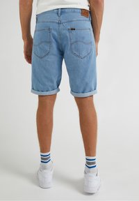 Ljusblå denimshorts med uppvikta fållar, med bakfickor och en brun läderetikett. Bärs med vita sneakers och randiga strumpor.