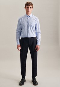 Lichtblauwe overhemd met knoopsluiting en borstzak, gecombineerd met donkere maatpakbroeken en zwarte veterschoenen. Soepele stof, aangesloten ontwerp.