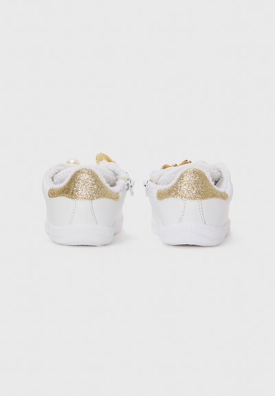 Baskets blanches avec des accents de paillettes dorées au niveau du talon et des colliers, présentant une doublure en tissu texturé et une semelle en caoutchouc lisse.