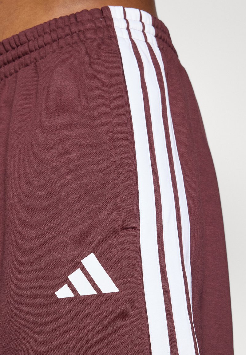 Pantalones cortos deportivos color burdeos con rayas verticales blancas a los lados. Cuentan con una cinturilla elástica y un pequeño logo blanco cerca del dobladillo.