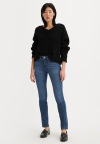 Maglione nero a maglia con scollo a V, abbinato a jeans blu slim-fit. L'outfit è completato da mocassini neri.