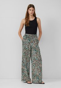 Top senza maniche nero abbinato a pantaloni larghi a fantasia nei colori nero, turchese e beige, dotati di tasche e dalla vestibilità rilassata.