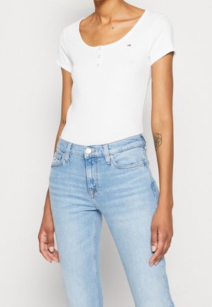 Witte bodysuit met korte mouwen, voorzien van een ronde hals en drie drukknoopsluitingen aan de voorkant, gecombineerd met lichtblauwe, licht beschadigde jeans.