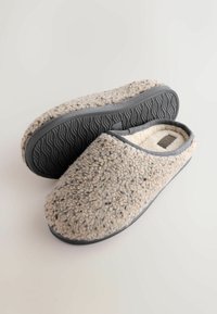 Beige fleece slippers with a textured surface, gray trim, and a rubber outsole featuring a wave pattern for grip. Open-back design.