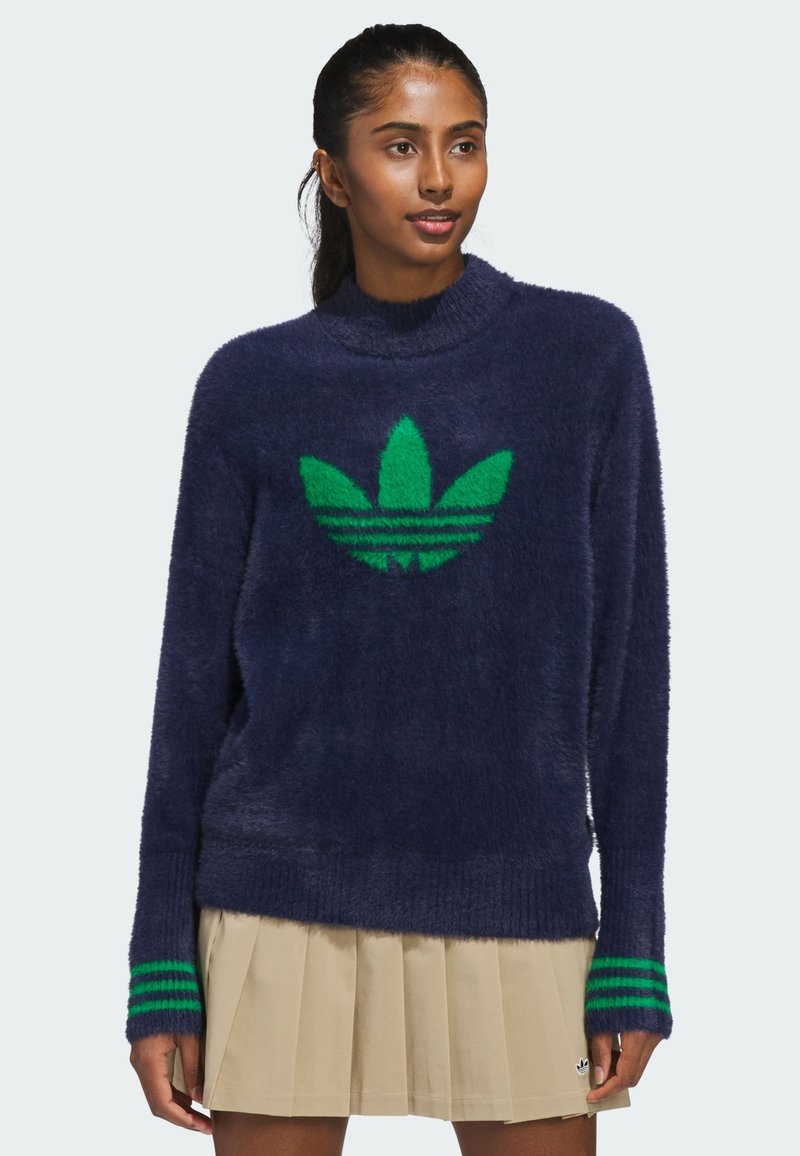 Marineblå fuzzy genser med grønn Adidas-logo og striper på ermer. Høy hals og avslappet passform, laget av mykt, strukturert materiale.