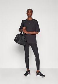 Svart trenings T-skjorte, svarte leggings og svarte joggesko med rosa detaljer. Bærer en svart treningsbag med teksturert design.