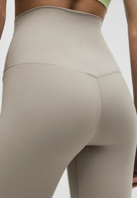 Hochtaillierte beigefarbene Leggings aus dehnbarem Material mit glatter Textur und subtiler Nahtdetailierung. Leichtgewichtiges und körperbetontes Design.