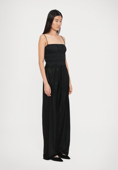 Costum negru în două piese, format dintr-un top ajustat cu spaghete plisate și pantaloni largi cu un finisaj texturat. Pantofi negri simpli, de tip slip-on.