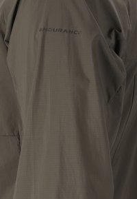 Gros plan sur un tissu vert olive avec le mot "ENDURANCE" imprimé en petites lettres majuscules sombres.