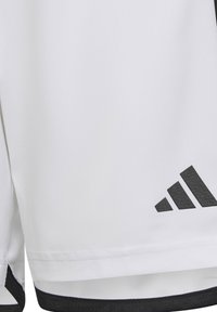 Shorts de sport blancs avec des accents noirs, fabriqués dans un tissu lisse et léger, et dotés d'un logo Adidas gris foncé sur le côté inférieur.