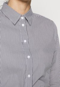 Napapaita, jossa on mustavalkoinen pystysig-pohja, terävä kaulus ja valkoiset napit etupuolella. Sileä kangas.