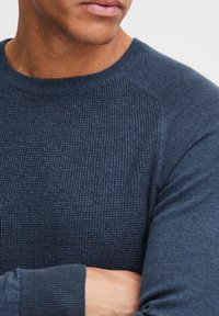 Marineblauer Strickpullover mit strukturiertem Rippenmuster, rundem Ausschnitt und eng anliegenden Bündchen, mit kontrastierenden glatten Ärmelakzenten.