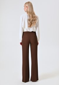 Pantaloni marroni a vita alta con gambe larghe, realizzati in tessuto liscio. La parte superiore è una blusa bianca con maniche lunghe, caratterizzata da una vestibilità comoda.
