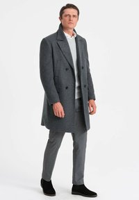 Grå dobbeltbrystet uldfrakke med spidse klapper, iført over en lys grå sweater og grå bukser, parret med sorte ankelstøvler.