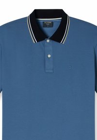 Polo bleu en tissu texturé. Présente un col noir avec des rayures blanches et dorées, deux boutons et un petit logo sur la poitrine.
