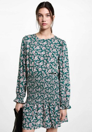 Blumenkleid aus grünem Stoff mit langen Ärmeln, rundem Ausschnitt und gerafftem Taillenbereich. Verfügt über einen Rüschensaum und ein pinkes Blumenmuster.