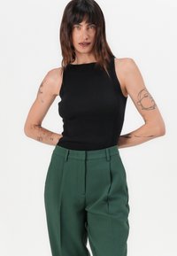 Black ribbed tank top paired with high-waisted green trousers. The top features a sleeveless design, and the pants have pleated detail.