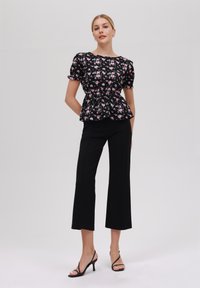 Svart blommig peplumtop med korta puffärmar; ihop med högmidjade svart cropped byxor och strappy svarta klackar.
