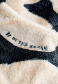 Kunstkarva kangas, millel on lehmamustriga must ja kreemjas värv, pehme tekstuur ja musta värvi trükitud tekst.