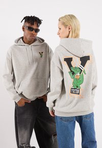 Grauer Hoodie mit einem Logo auf der Vorderseite und einem großen grünen Krokodil-Graphic auf der Rückseite mit dem Text "YRTN." Weicher Stoff, lockere Passform, Kapuze mit Kordelzug.