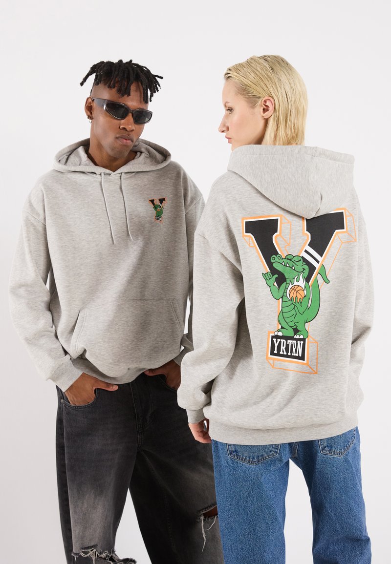 Grauer Hoodie mit einem Logo auf der Vorderseite und einem großen grünen Krokodil-Graphic auf der Rückseite mit dem Text "YRTN." Weicher Stoff, lockere Passform, Kapuze mit Kordelzug.