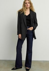 Blazer double boutonné à rayures noires sur un topper noir à encolure en V, associé à un jean flare sombre et des ballerines à bout pointu noires.